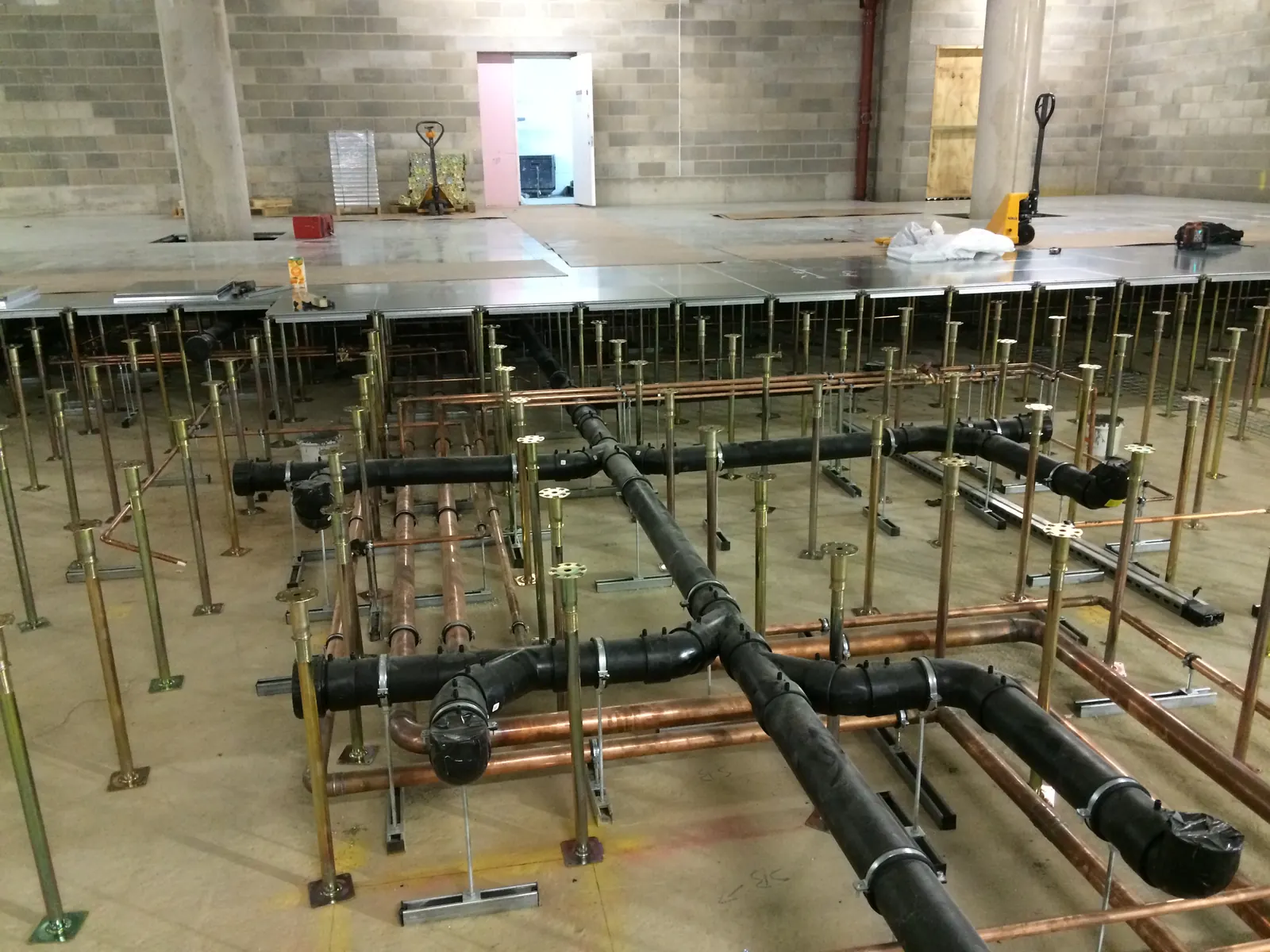 AELTC Wimbledon — below-floor pipework installation detail, complex services coordination in confined basement