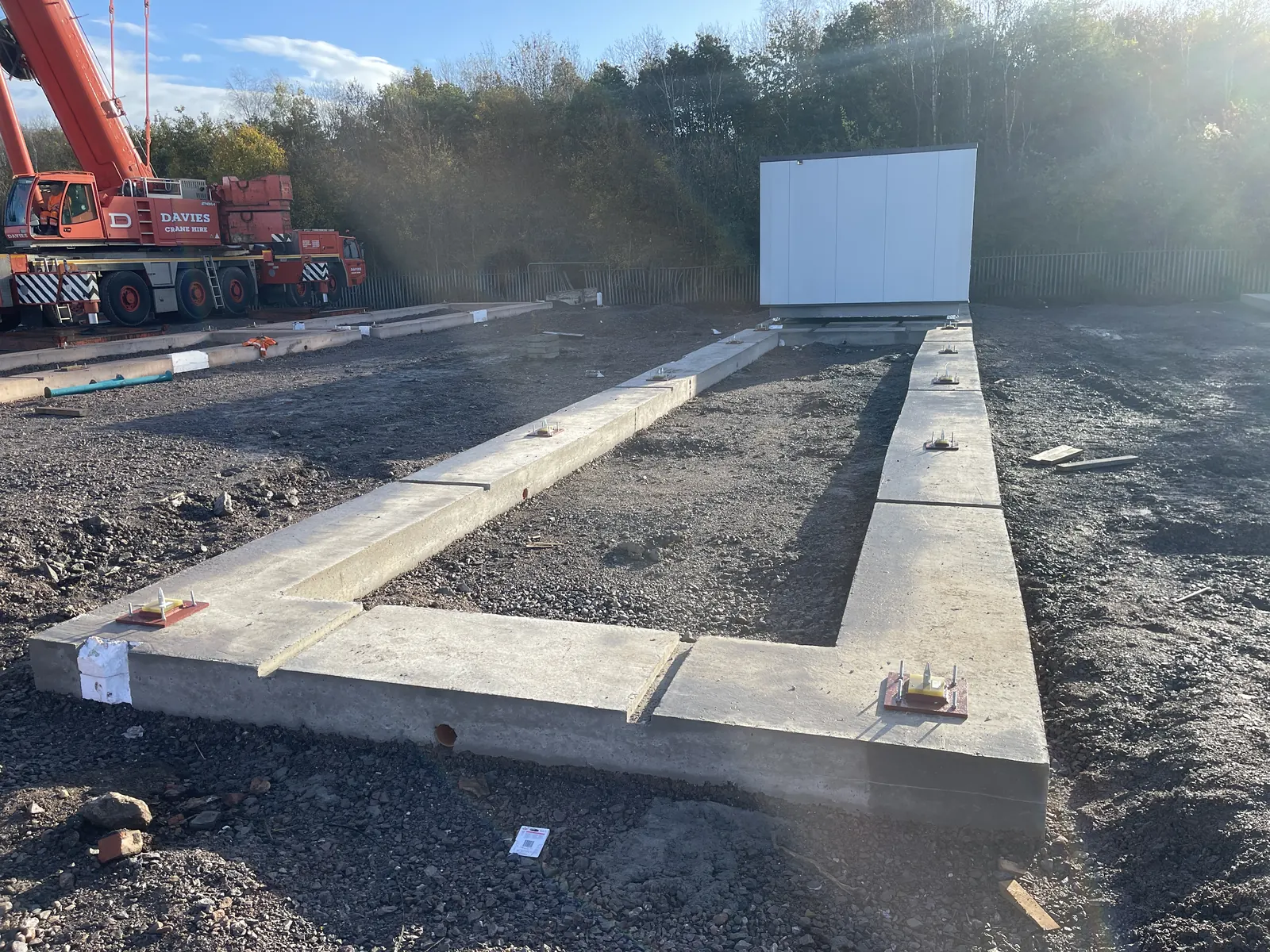 Craig Garbutt — MMC site groundworks: precast concrete foundation frame set out ready to receive a modular volumetric unit, mobile crane on standby