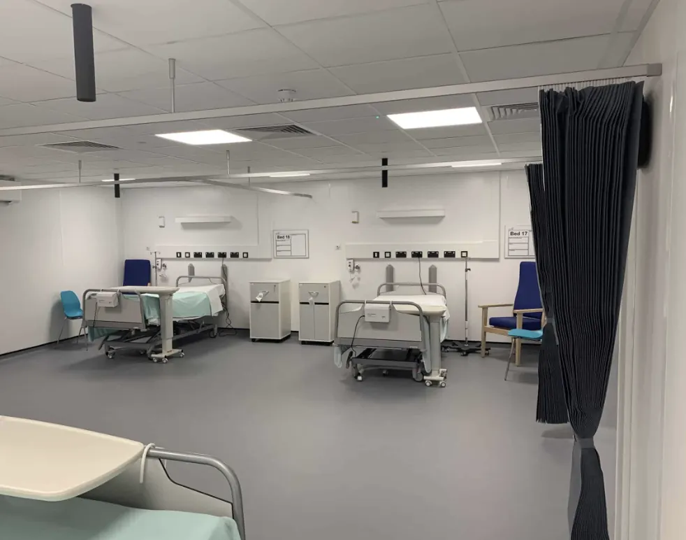 Completed MMC modular ward interior delivered by Craig Garbutt at a live NHS hospital — offsite-manufactured ward units with beds and clinical equipment, connected to the existing hospital via a newly built transfer corridor